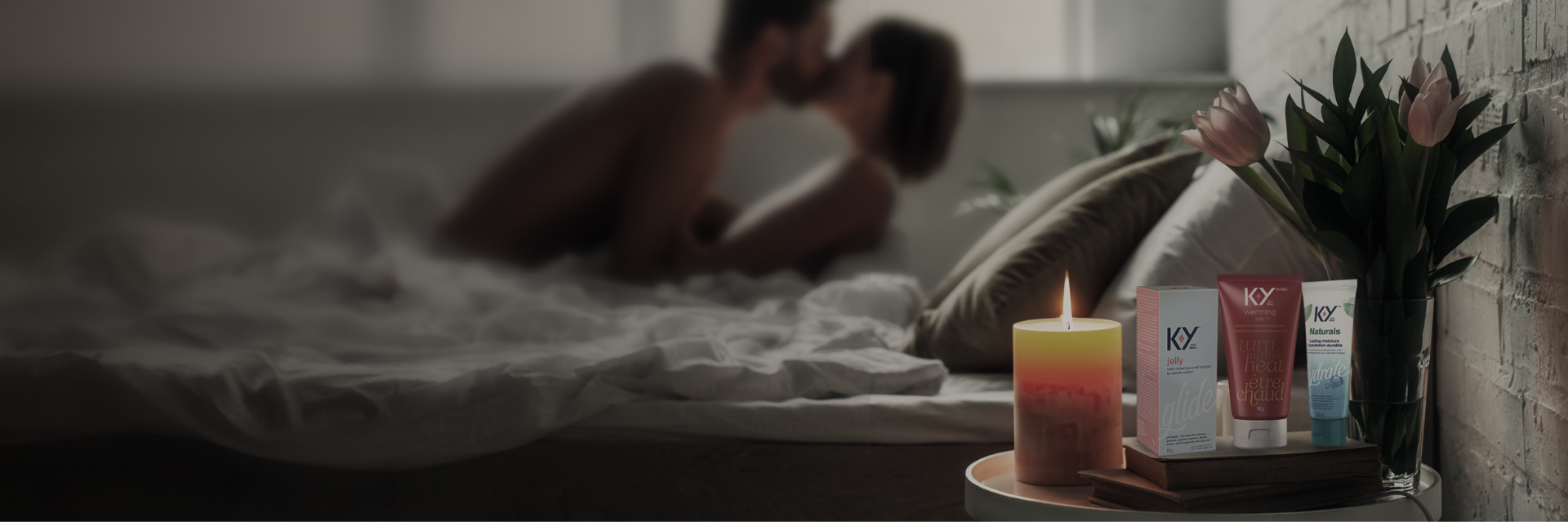 A couple kissing in bed next to a lit candle and flowers beside the K-Y® Lubricant - Warming® Gel, K-Y® Lubricant - Gel, and K-Y® Lubricant - Naturals® Moisture+ Intimate Gel.