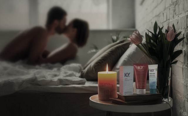 A couple kissing in bed next to a lit candle and flowers beside the K-Y® Lubricant - Warming® Gel, K-Y® Lubricant - Gel, and K-Y® Lubricant - Naturals® Moisture+ Intimate Gel.