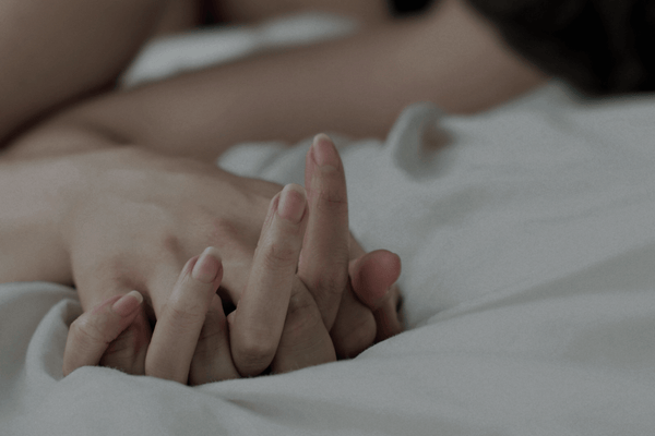 Couple dans un lit avec une main appuyée sur le lit.