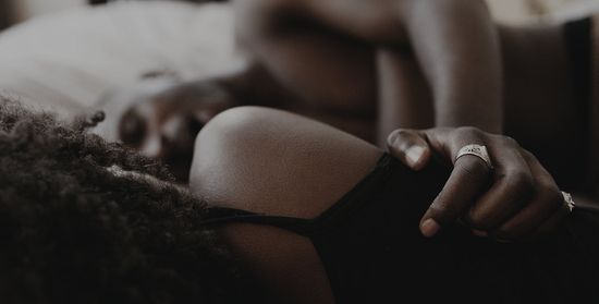Two partners wearing black clothing clutching onto one another while lying down in bed.