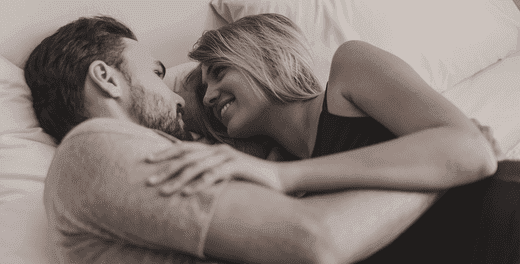 Un couple étendu au lit et se regardant dans les yeux.